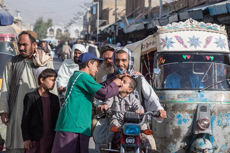 A young male volunteer in Afghanistan drops polio vaccination in a small boy's mouth as he passes by on a motorcyle