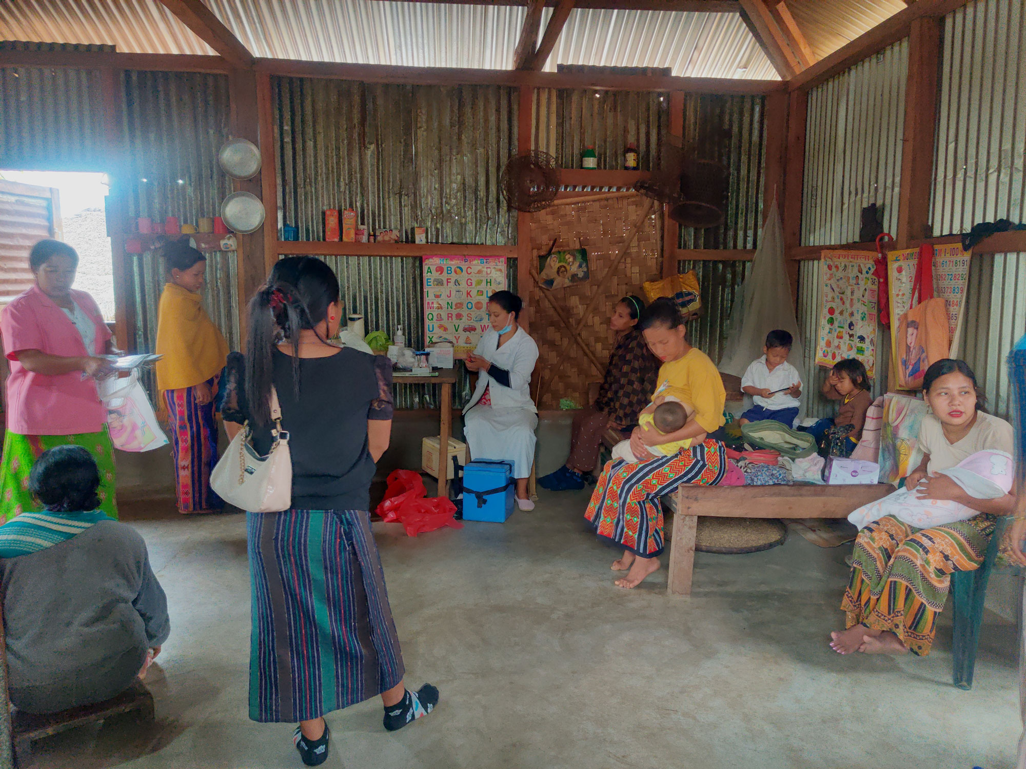 Ms Lipi Pegu, auxiliary nurse midwife from Community Health Centre Kanubari (centre, in white), setting up a temporary immunization and health clinic in the Chopnu Community Centre kitchen