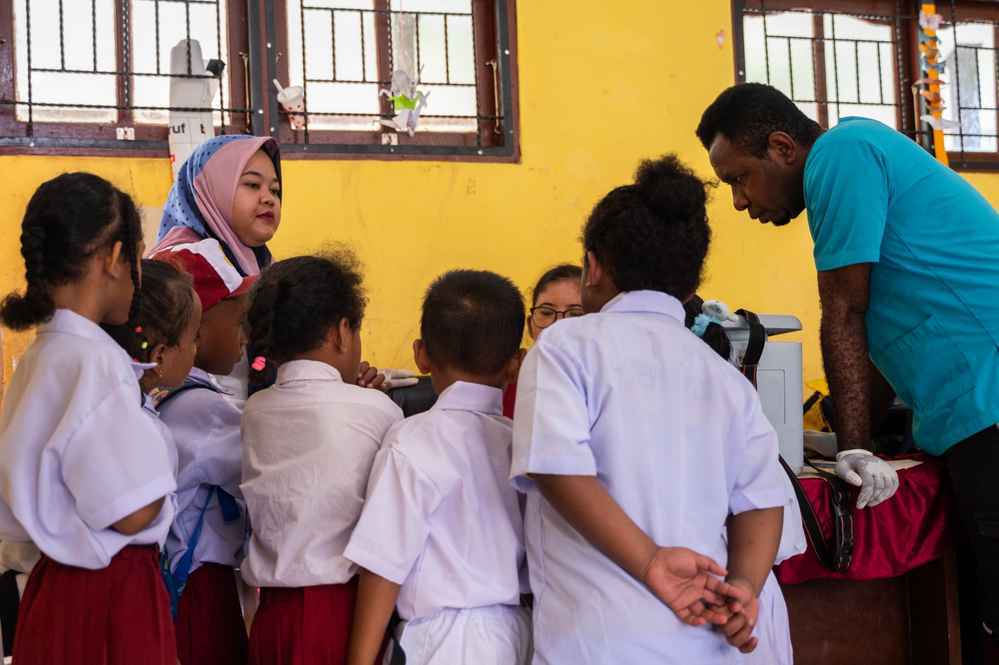 A group of students in uniforms gathered around health care workers who are preparing for polio vaccination